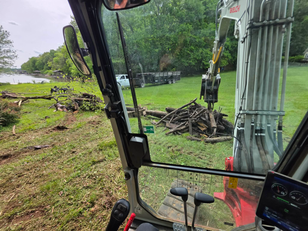 View from excavator cab of debris pile on lakefront property during storm damage tree removal – White's Tree Service East Tennessee